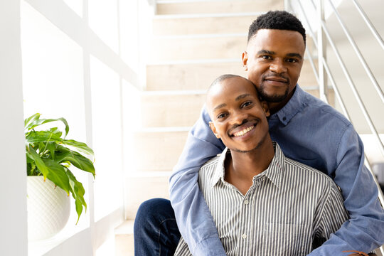 Portrait of smiling african american young gay couple dressed in formals sitting on steps at home