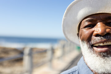 Portrait of happy senior african american man with sun hat on promenade at seaside