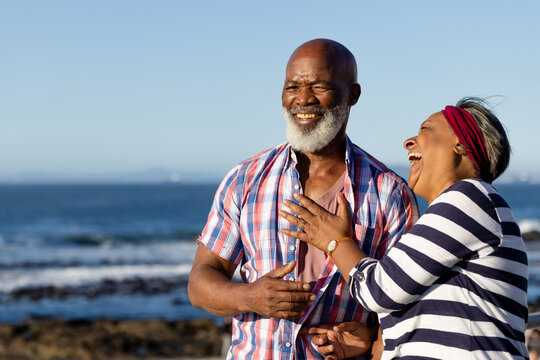 Happy senior african american couple embracing and laughing at seaside