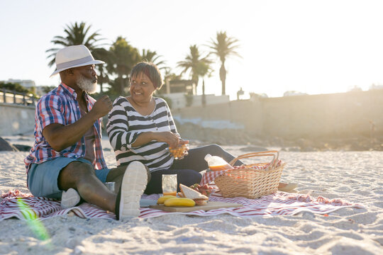Happy senior african american couple having picnic and eating fruit at beach