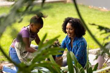 Happy african american mother and daughter planting flowers together in garden