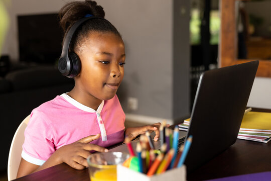 Happy african american daughter in headphones listening during online lesson using laptop at home