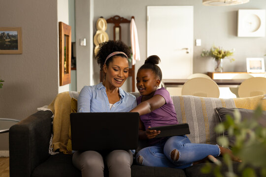 Happy African American Mother And Daughter Using Laptop Together Sitting On Couch At Home