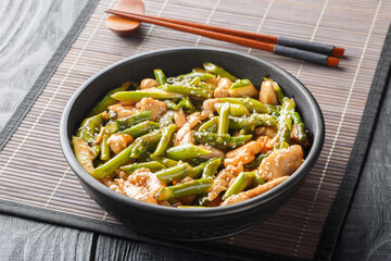 Asian style fried chicken fillet with asparagus in soy sauce close-up in a bowl on the table....