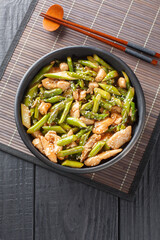 Asian healthy stir fry chicken fillet with asparagus closeup in a bowl on the table. Vertical top view from above