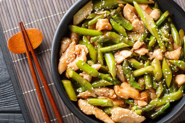 Chinese stir-fried chicken fillet with asparagus and sesame close-up in a bowl on the table. Horizontal top view from above