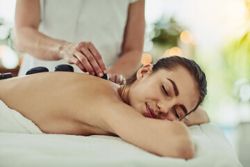 Fototapeta na wymiar Health, relax and woman getting a hot stone back massage at spa for luxury, calm and natural self care. Beauty, body care and tranquil female person sleeping while doing rock body treatment at salon.