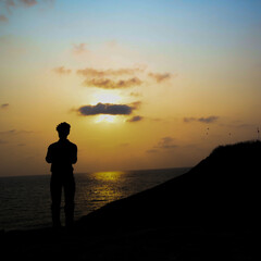 the silhouette image of a sad boy standing near an ocean with sky in the background