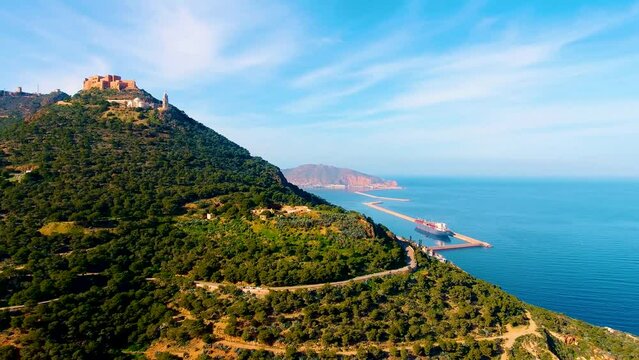 cityscapes of the santa cruz chapel at the top of the mountain at sunset with beautiful orange and blue colors and the sea in the background Algeria