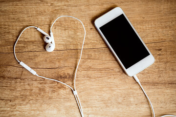 Close-up of smart phone with headphones on a wooden background. (Top view). Listen to music