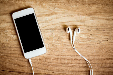 Close-up of smart phone with headphones on a wooden background. (Top view). Listen to music