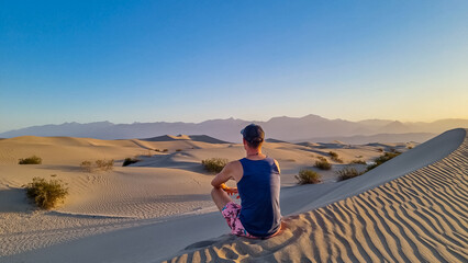 Fototapeta premium Touristic man enjoying the sunrise with scenic view on Mesquite Flat Sand Dunes, Death Valley National Park, California, USA. Morning walk in Mojave desert with Amargosa Mountain Range in back.