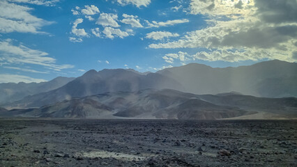 Panoramic sunrise view of the silhouette of Black, Amargosa and Panamint Mountain Range in Death Valley National Park, California, USA. Hot air and morning atmosphere in the Mojave desert. Sunbeams