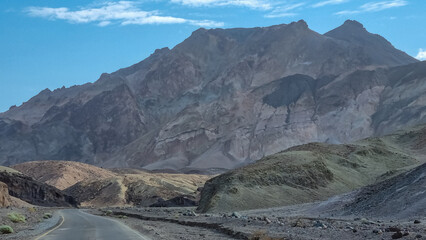 Panoramic view of endless empty road leading to colorful geology of multi hued Artist Palette rock formations in Death Valley National Park near Furnace Creek, California, USA. Black mountains