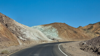 Panoramic view of endless empty road leading to colorful geology of multi hued Artist Palette rock formations in Death Valley National Park near Furnace Creek, California, USA. Black mountains