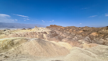 Fototapeta na wymiar Scenic view of Badlands of Zabriskie Point, Furnace creek, Death Valley National Park, California, USA. Erosional landscape of multi hued Amargosa Chaos rock formations, Panamint Range in the back