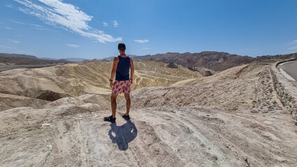 Man with scenic view Badlands of Zabriskie Point, Furnace creek, Death Valley National Park, California, USA. Erosional landscape of multi hued Amargosa Chaos rock formations, Panamint Range in back