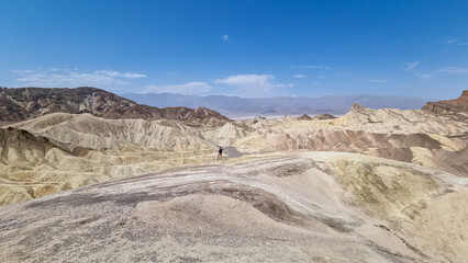 Fototapeta na wymiar Man with scenic view Badlands of Zabriskie Point, Furnace creek, Death Valley National Park, California, USA. Erosional landscape of multi hued Amargosa Chaos rock formations, Panamint Range in back