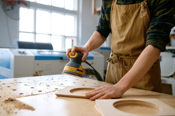 Man carpenter polishing bar planks with eccentric grinding machine