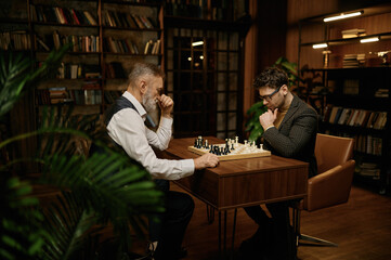 Senior man and young chess player having friendly match at home