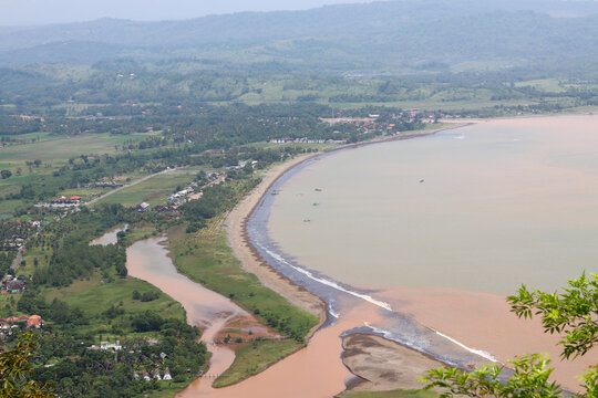 Turbid waters of the Ciletuh Geopark bay stretch along the rugged coastal landscape.