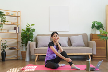 Sporty woman sits on yoga mat and smiling after watching yoga training online to exercise at home