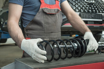 An auto mechanic holds a new shock absorber strut and a spring in his hands. The specialist...