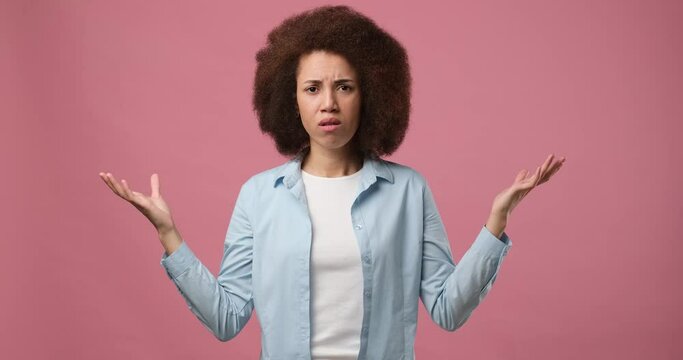 Emotional incomprehensible african american woman shrugging shoulders and raising hands asking Why standing over pink studio background