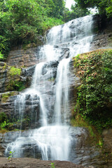 Fototapeta na wymiar Beautiful hidden waterfall in mountains. Slow shutter speed. Waterfall portrait