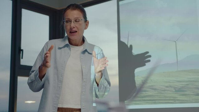 Female team leader explaining presentation about wind farm on projection screen to colleagues during business meeting in renewable energy company in the office. Medium shot