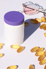 white plastic bottle with pills and sunglasses on white background. template, mock up concept. copy space. sun protection and sunscreen supplements