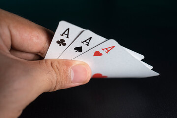 man hand holding and peeking his triple aces of playing cards on black background