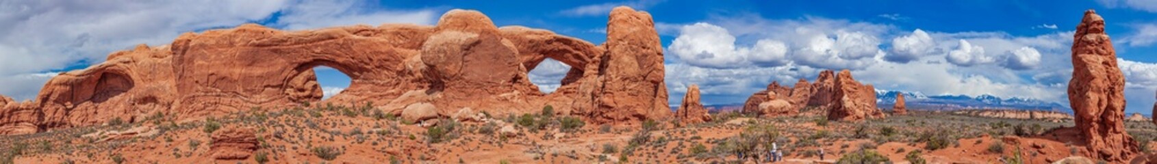 Fototapeta na wymiar Panoramic view of North Window, South Window, and Turret Arch with beautiful clouds in the sky, small figures of people in the frame emphasize the scale and beauty of this majestic creation, Moab, USA
