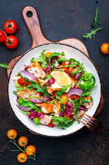 Gourmet salad with grilled salmon with tomatoes, cucumber, arugula, radicchio, red onion and lettuce with lemon oil dressing. Healthy lunch. Brown stone table background, top view