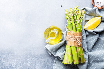 Fresh asparagus bunch, salt, pepper, lemon and olive oil on gray stone kitchen table background,...