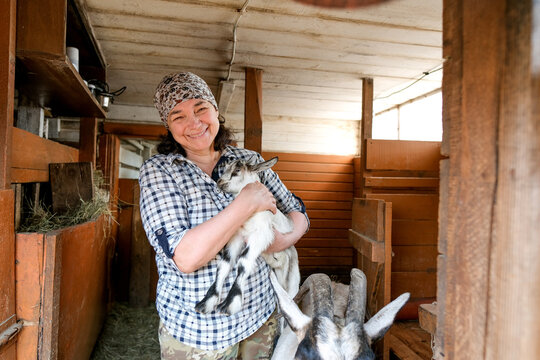 Female farmer snuggling baby alpine goat in hands. Cute baby goat portrait.