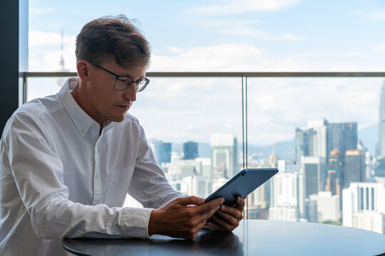 Man in glasses using tablet at table in panoramic office - Powered by Adobe