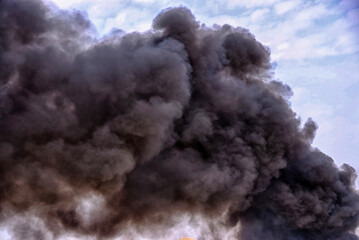 Nature pollution after burning rubber tires of car wheels, which caused black smoke to fly in the sky and mix with clouds
