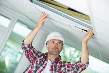 man in builder uniform hand up installing suspended ceiling