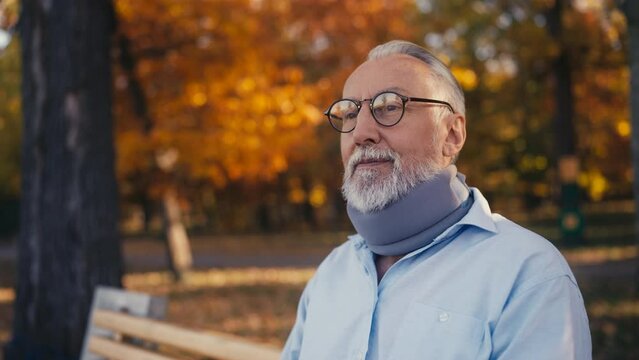 Elderly man wearing neck collar brace enjoying view in a park, senior lifestyle