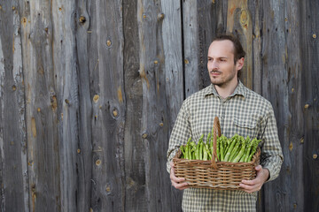 Young farmer holding big basket of green asparagus