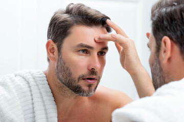 Close-up portrait of perfect brunet man touching chin and skin. Handsome man touching face in front of the mirror in bath. Perfect skin. Man cosmetic, skin treatment. Hygiene and skin care male face.