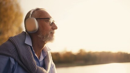 Senior man putting headphones on to listen to music by the lake, meditation