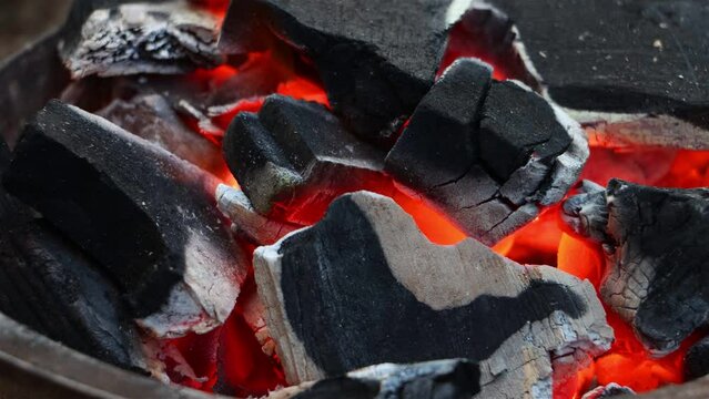 The charcoal glows red in the fire pit for the grill, close up