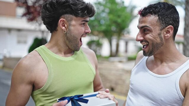 Two men couple smiling confident surprise with birthday gift at street