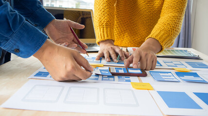 Close-up ux developers and ui designers use augmented reality to brainstorm on mobile app interface wireframe designs on modern office desks. Creative digital development office