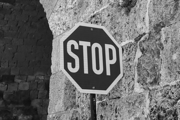 Black and white stop sign on a pole against a brick stone background wall. Communication and safety...