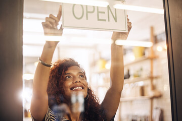 Open, sign and happy woman at window of shop, store and notice of retail shopping time, board and...