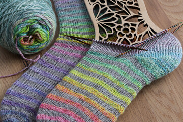 Beautiful pair of handknit socks with a nice rainbow stripes pattern knitted from handspun sockwool, hot on the needles with a wooden background 	