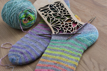 Beautiful pair of handknit socks with a nice rainbow stripes pattern knitted from handspun sockwool, hot on the needles with a wooden background 	